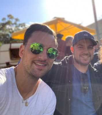 Zwei Mitarbeitende an einem sonnigen Tag im Freien. Im Hintergrund ist ein Stand mit Sonnenschirm.