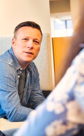 Ein männlicher Mitarbeitender hört einer Kollegin zu.