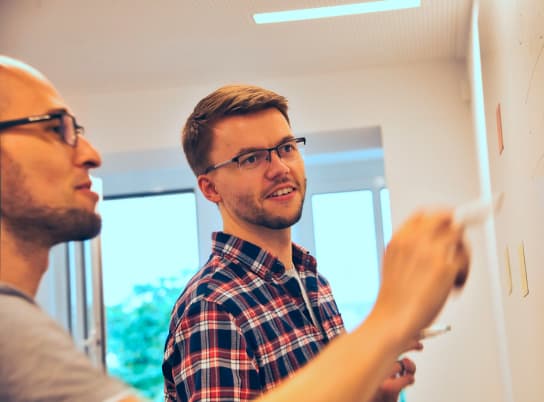 Zwei Mitarbeitende stehen vor einem Whiteboard und notigeren gemeinsam Ideen.